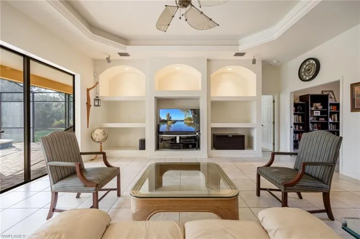 Living room featuring a tray ceiling, ceiling fan, built in features, and light tile patterned floors
