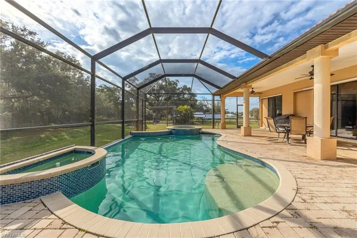 View of pool featuring a lanai, a patio area, and in-ground hot tub.