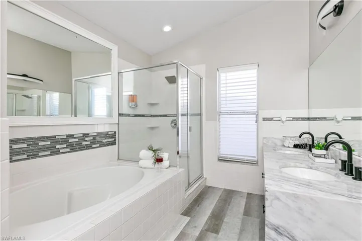 Bathroom featuring double vanity, a bath, a shower stall, light wood-style floors, and tile walls
