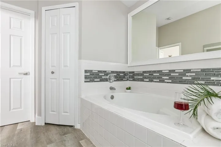Bathroom featuring a closet, a bath, and light wood finished floors