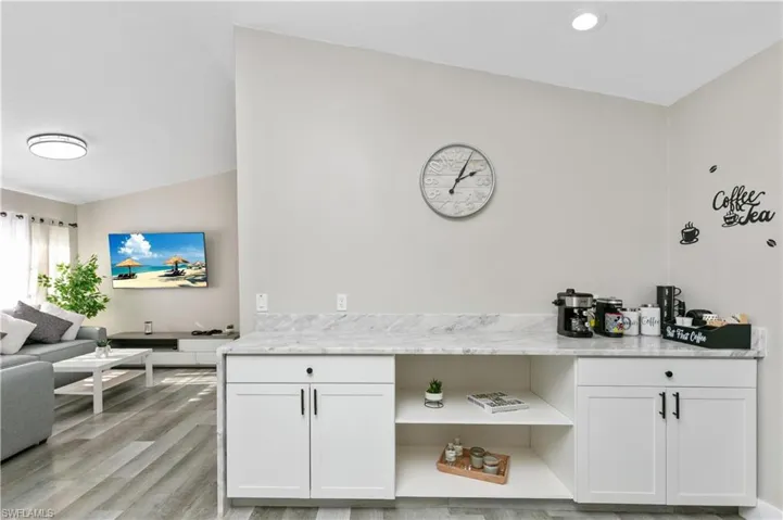 Bar area featuring white cabinets, light stone countertops, light wood-style flooring, and open shelves