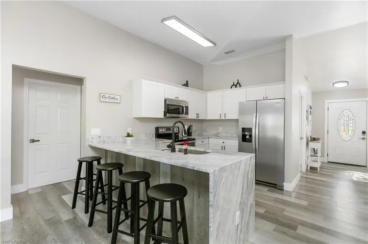 Kitchen with light stone counters, a breakfast bar, stainless steel appliances, a peninsula, and white cabinets