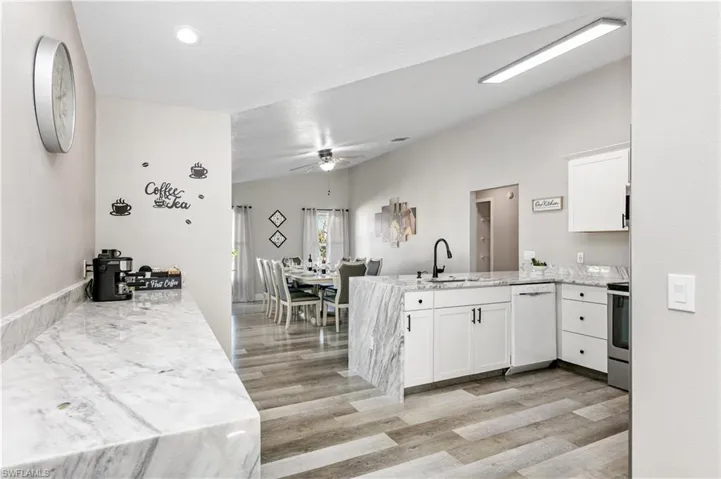 Kitchen featuring a peninsula, light stone counters, white cabinetry, white dishwasher, and light wood-type flooring