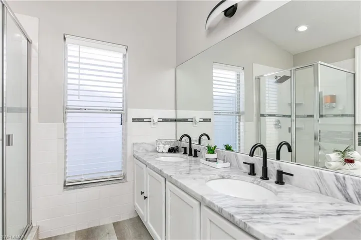 Full bathroom featuring a shower stall, double vanity, light wood-style floors, a wainscoted wall, and tile walls