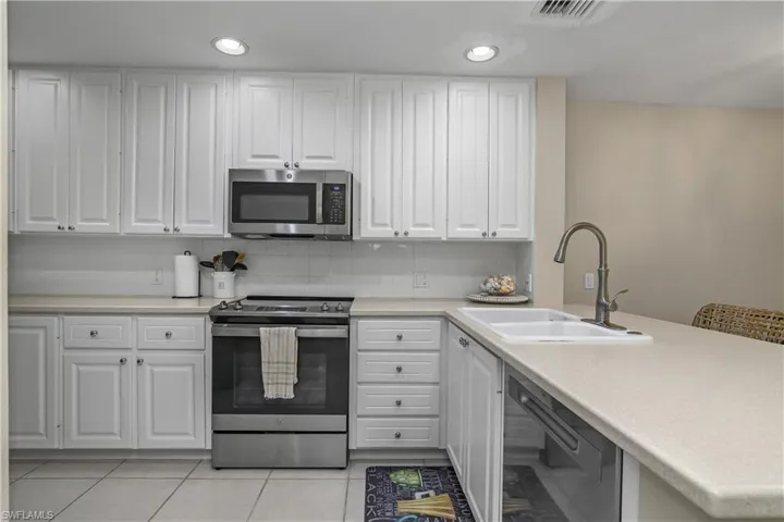 Kitchen with stainless steel appliances, tasteful backsplash, light countertops, white cabinets, and recessed lighting