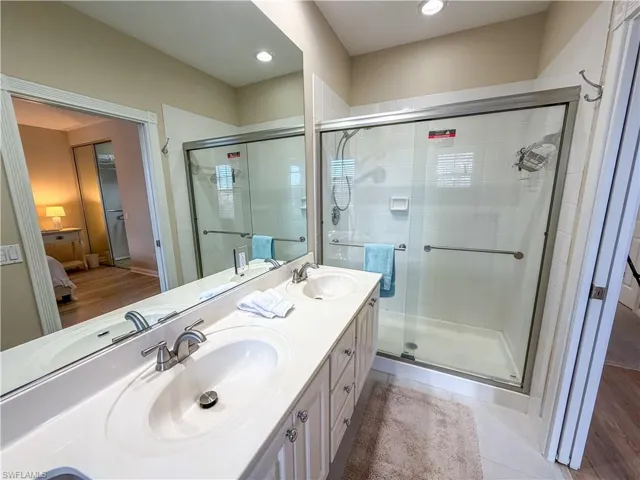 Ensuite bathroom featuring double vanity, a shower stall, and light tile patterned floors