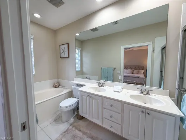 Bathroom featuring double vanity, light tile patterned floors, ensuite bath, a garden tub, and a shower stall