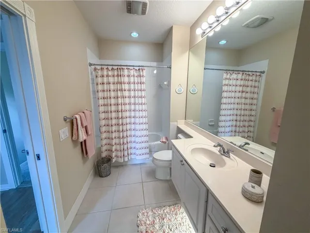 Bathroom with vanity, shower / bathtub combination with curtain, light tile patterned flooring, and a textured ceiling