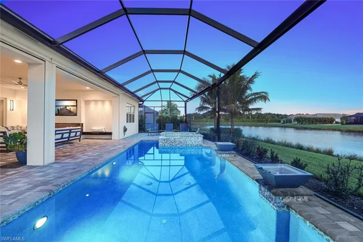 Pool at dusk with a patio area, a water view, and a lanai