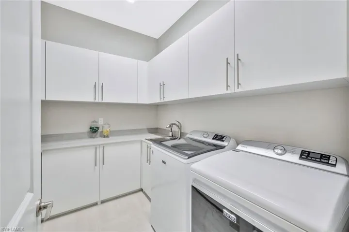Laundry room with sink, cabinets, washer and clothes dryer, and light tile patterned floors