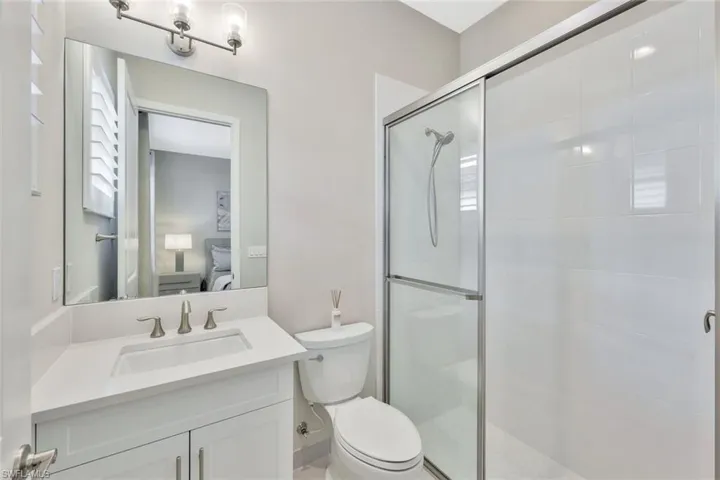 Bathroom featuring a shower with door, toilet, and vanity
