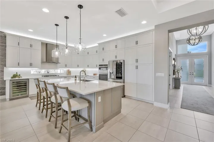 Kitchen with stainless steel appliances, a center island with sink, beverage cooler, and wall chimney exhaust hood