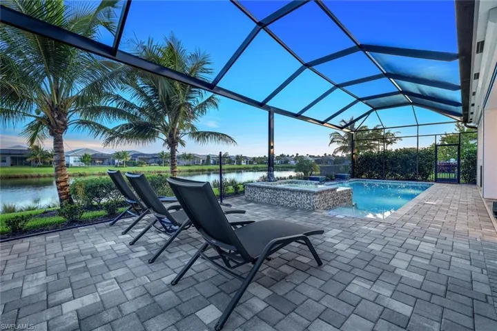 Pool at dusk with a patio area, an in ground hot tub, a water view, and screen enclosure