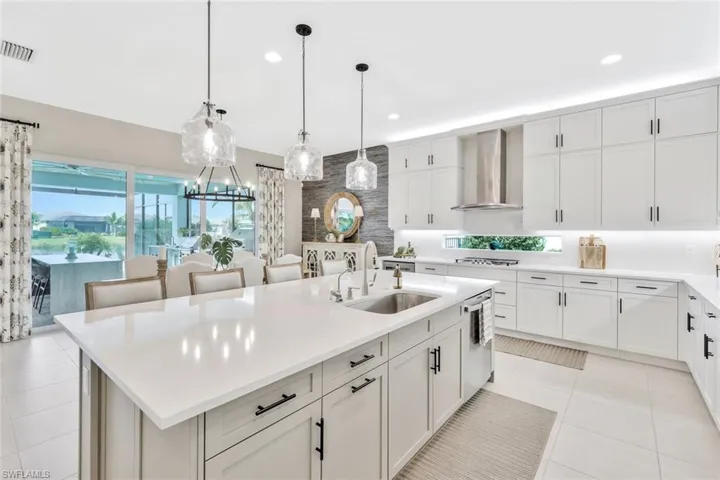 Kitchen featuring light tile patterned flooring, pendant lighting, wall chimney exhaust hood, and an island with sink