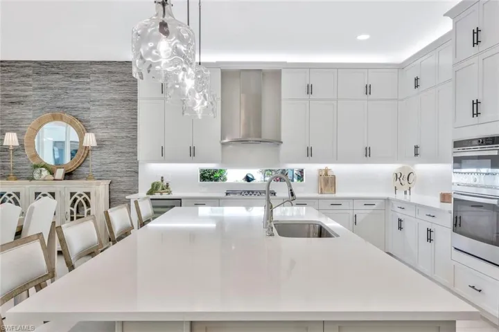 Kitchen featuring a kitchen island with sink, stainless steel appliances, wall chimney exhaust hood, pendant lighting, and sink
