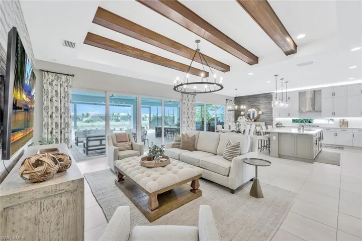 Living room featuring light tile patterned flooring, a chandelier, and beamed ceiling