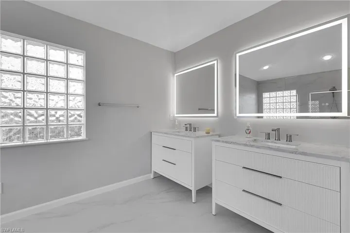 Bathroom with two vanities, walk in shower, comfort height toilet and light marble finish flooring