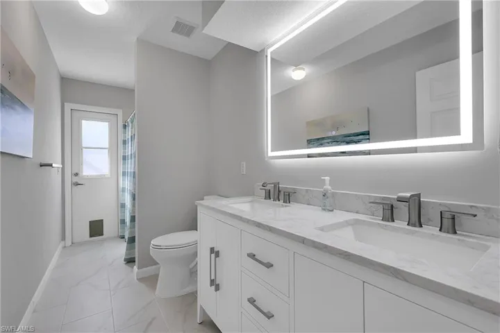 Hall bath matches the primary bath, featuring double vanity, curtained shower/tub, cabana door to pool area and light marble finish floors