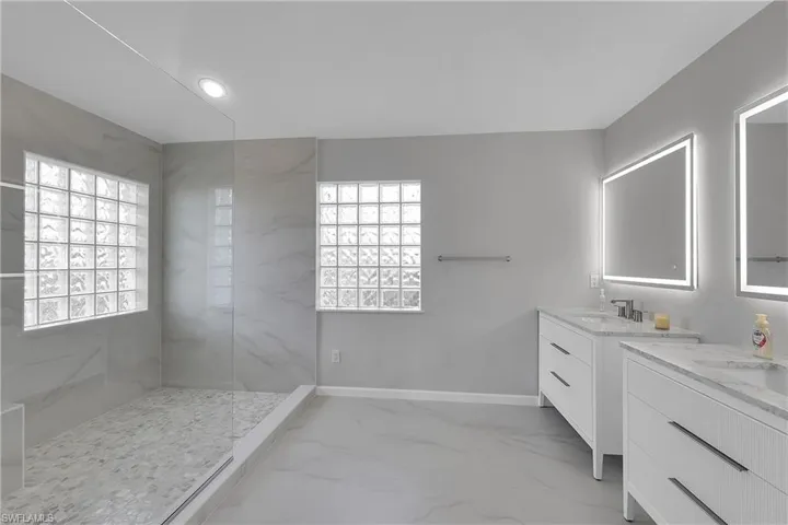 Brand new bathroom featuring a marble finish shower, linear drain, two vanities, recessed lighting, and light marble finish floors