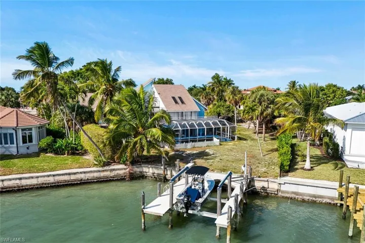 Dock area with boat lift, a water view, a lanai, and a yard
