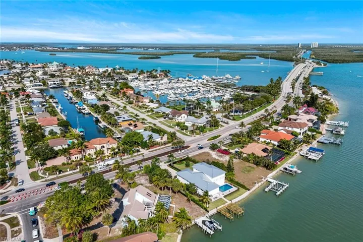 Aerial view of property and surrounding area featuring a large body of water, a marina, and nearby suburban area