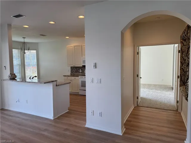 Kitchen with white cabinetry, light hardwood / wood-style floors, stone countertops, white appliances, and decorative backsplash
