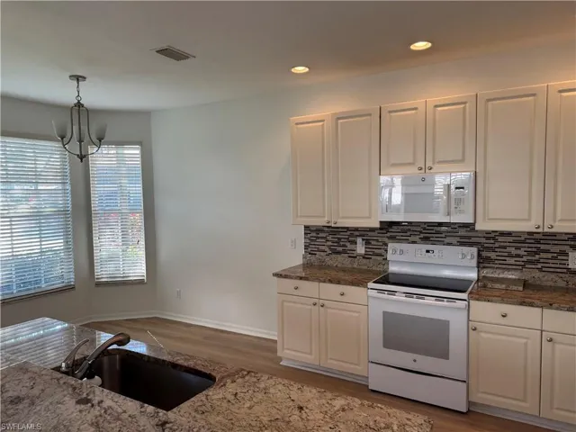 Kitchen featuring white cabinetry, decorative light fixtures, and white appliances