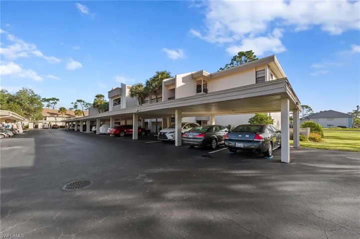 Multi-story building exterior featuring a covered carport and paved parking surface