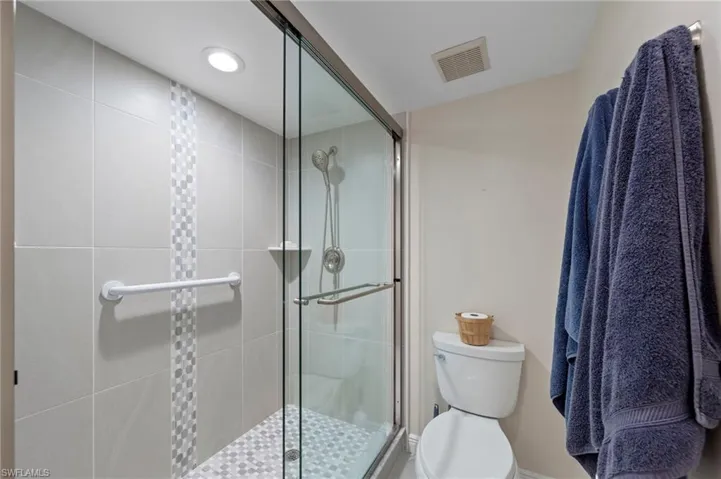 Walk-in shower featuring a sliding glass door, a decorative mosaic tile accent stripe, a handheld shower fixture, and a wall-mounted safety bar
