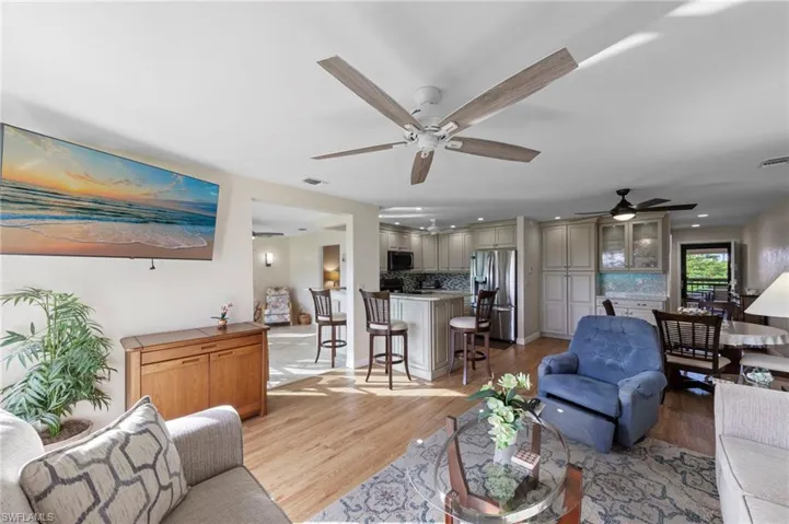 Open-concept interior featuring wood-finish flooring, recessed lighting, ceiling fans with integrated light kits, kitchen cabinetry with glass-front display accents, and a central kitchen island