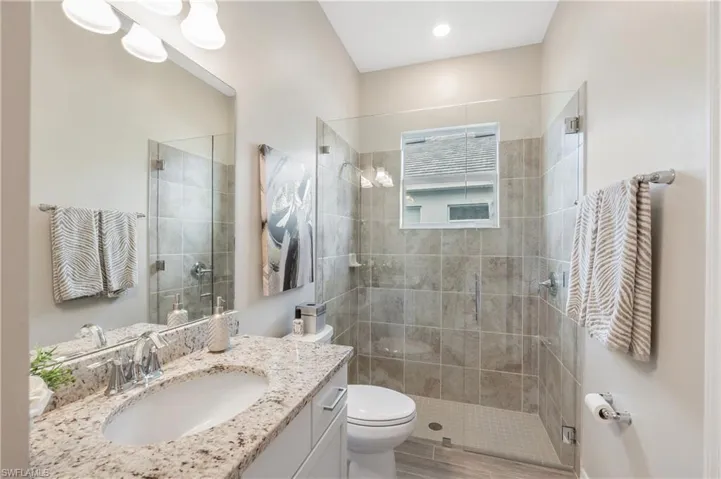 Bathroom featuring wood-type flooring, vanity, toilet, and a shower with door