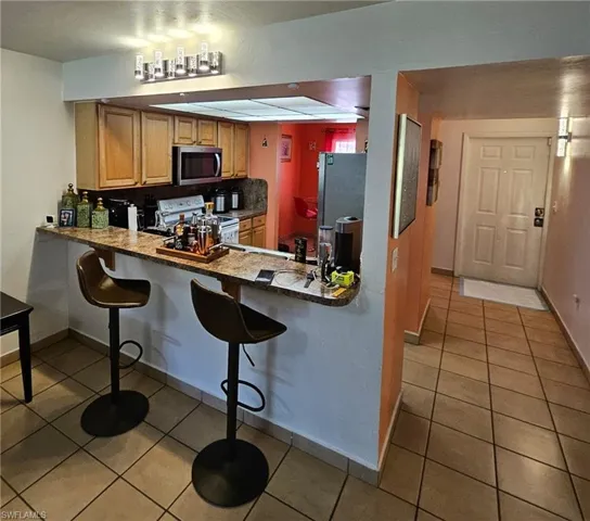 Kitchen featuring a breakfast bar area, light tile patterned floors, kitchen peninsula, backsplash, and stainless steel appliances