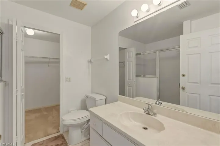 Bathroom featuring vanity, a shower stall, a walk in closet, light colored carpet, and light tile patterned floors