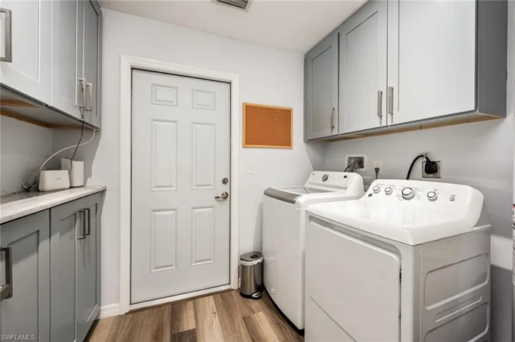Laundry area with light hardwood / wood-style floors, washing machine and clothes dryer, and cabinets
