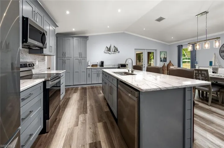 Kitchen with wood-type flooring, a kitchen island with sink, sink, vaulted ceiling, and stainless steel appliances