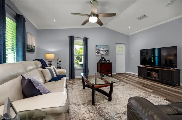 Living room with wood-type flooring, crown molding, vaulted ceiling, and ceiling fan
