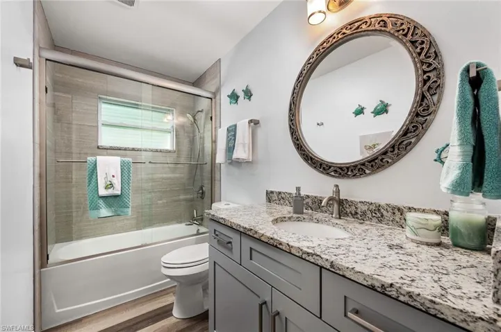 Full bathroom featuring hardwood / wood-style floors, shower / bath combination with glass door, toilet, and vanity