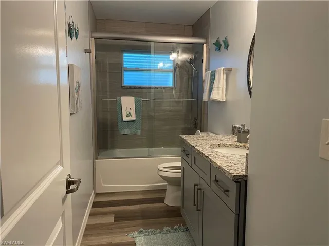 Full bathroom featuring vanity, toilet, wood-type flooring, and bath / shower combo with glass door
