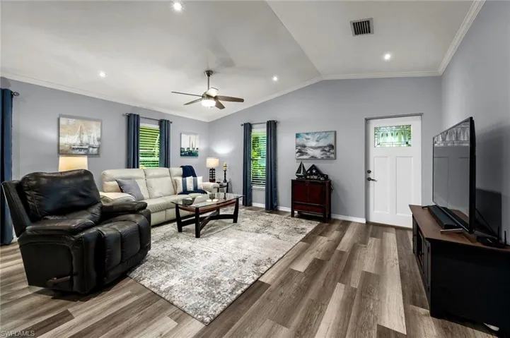 Living room with a wealth of natural light, lofted ceiling, hardwood / wood-style floors, and crown molding