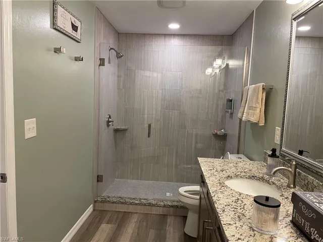 Bathroom featuring hardwood / wood-style flooring, vanity, toilet, and an enclosed shower
