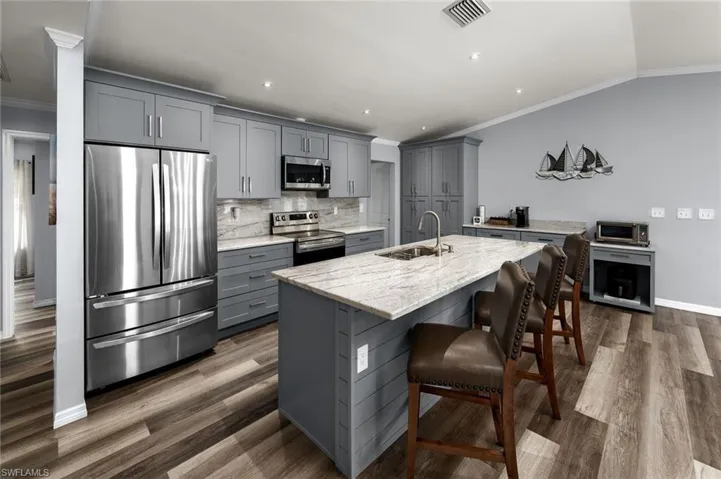 Kitchen with sink, an island with sink, gray cabinetry, stainless steel appliances, and dark hardwood / wood-style flooring