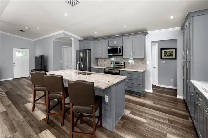 Kitchen featuring gray cabinetry, stainless steel appliances, a center island with sink, and dark wood-type flooring