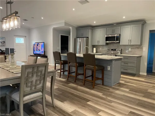 Kitchen with appliances with stainless steel finishes, light hardwood / wood-style floors, gray cabinets, and a center island with sink