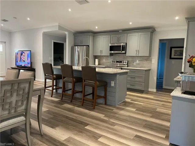 Kitchen featuring gray cabinetry, a kitchen island with sink, light wood-type flooring, and appliances with stainless steel finishes