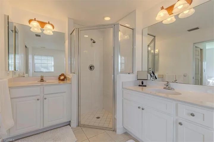 Full bath featuring two vanities, a shower stall, and light tile patterned flooring