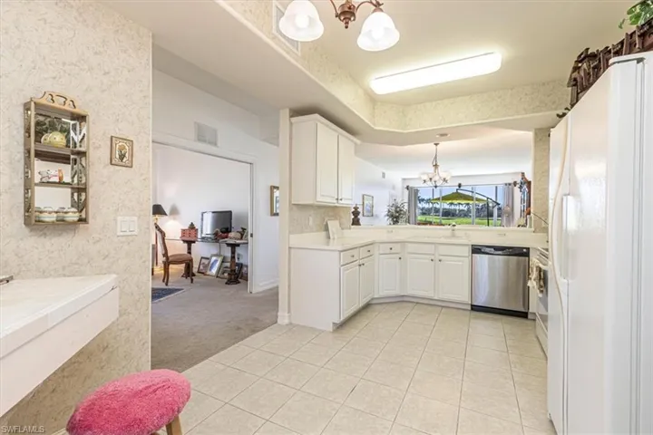 Kitchen featuring a chandelier, light carpet, stainless steel appliances, decorative light fixtures, and white cabinets
