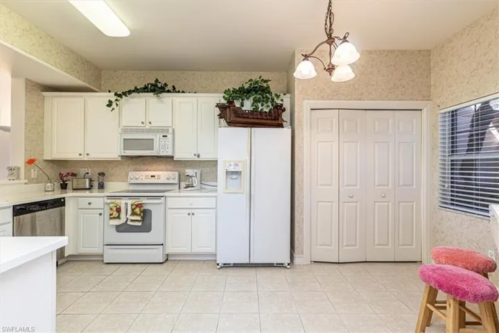 Kitchen with wallpapered walls, white appliances, decorative light fixtures, light countertops, and a chandelier