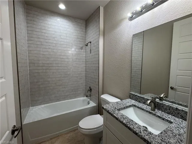 Full bathroom featuring vanity, tiled shower / bath combo, toilet, and tile patterned flooring