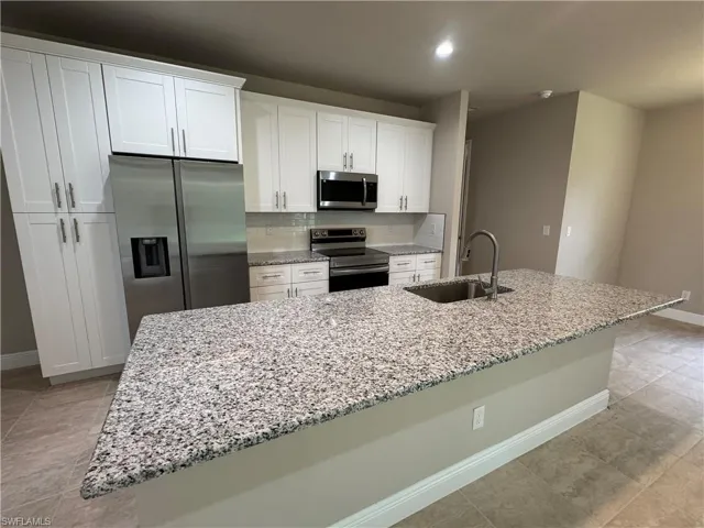 Kitchen with a center island with sink, sink, appliances with stainless steel finishes, and white cabinets