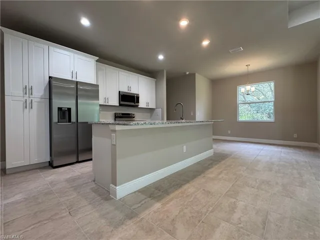 Kitchen featuring stainless steel appliances, light stone countertops, a center island with sink, and white cabinets